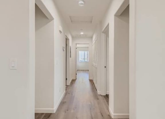 A long, narrow hallway with white walls and wood flooring.