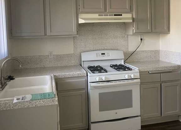 A kitchen with a white stove and cabinets.