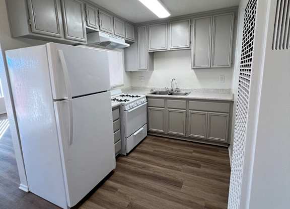 A white refrigerator is in a kitchen with wooden floors.