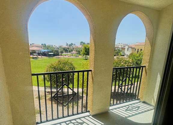 A balcony with a black railing and a view of a green lawn and buildings.
