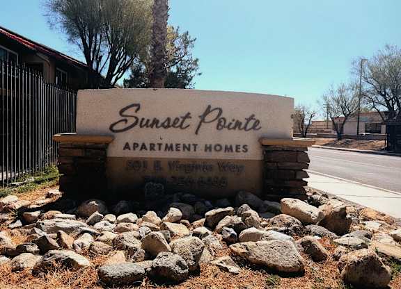 A sign for Sunset Pointe Apartment Homes sits in front of a fence and trees.