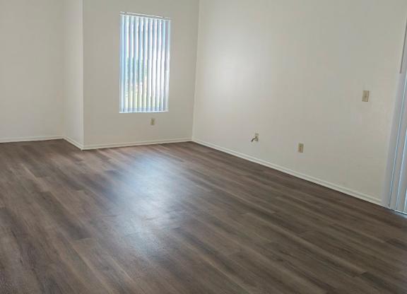 A room with wooden flooring and a window with blinds.