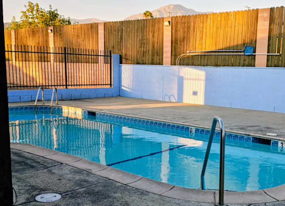 A small pool with a diving board and a metal fence.