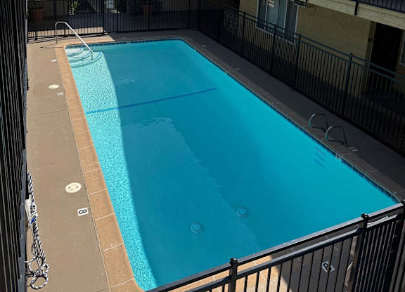 A small pool in a courtyard surrounded by a black fence.
