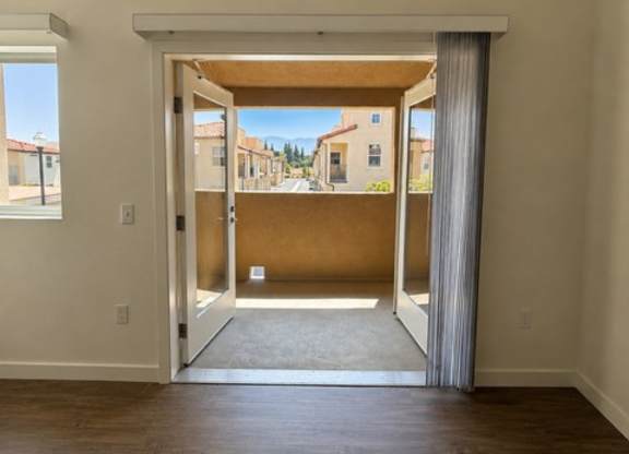 A room with a wooden floor and a view of a street through a sliding glass door.
