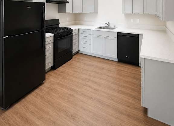 A black refrigerator is in a kitchen with wooden floors and white walls.