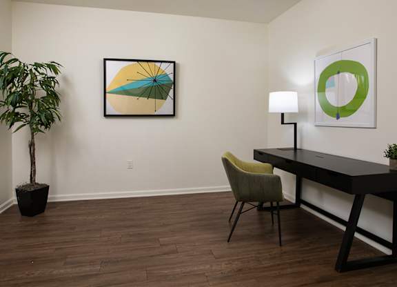 A room with a desk, chair, and two pictures on the wall.
