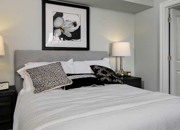 A cozy, well-appointed bedroom with a grey upholstered headboard and direct access to an en-suite bathroom in these luxury Rittenhouse Square apartments Philadelphia PA.