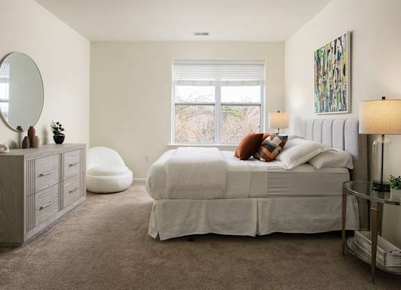 A bedroom with a large bed, a round mirror, and a painting on the wall.