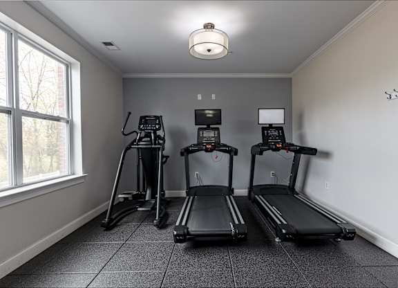 Modern fitness center at Queens Gate Apartments featuring treadmills with built-in screens and an elliptical, designed to support your active lifestyle.