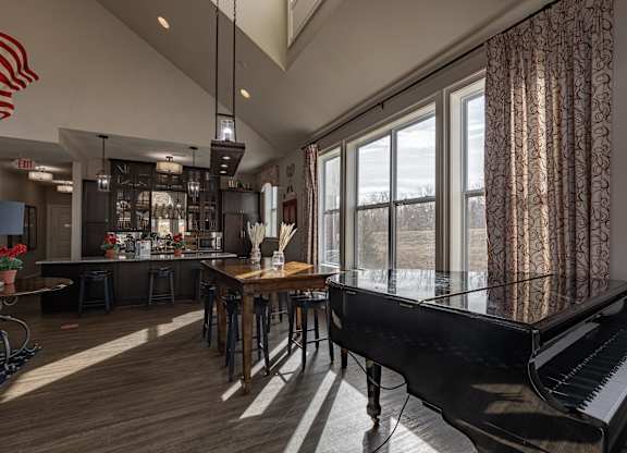 Elegant clubhouse at Queens Gate Apartments featuring natural light, a grand piano, communal dining tables, and a modern bar area.