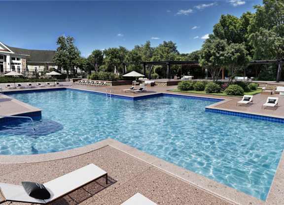 A large swimming pool with a hot tub and lounge chairs.