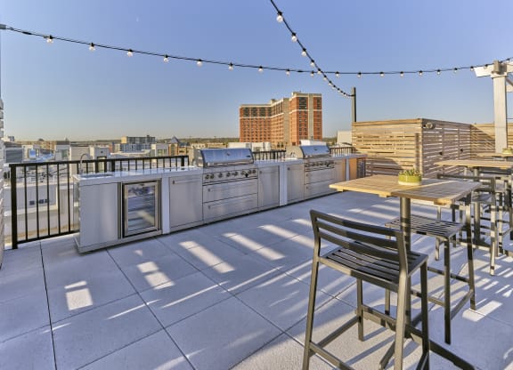 Spacious rooftop grill area at The Mint Rahway featuring stainless steel grills, refrigerators, and string lights, perfect for social gatherings and enjoying views