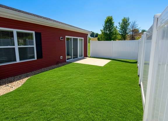 A red building with a white fence and green grass in front.
