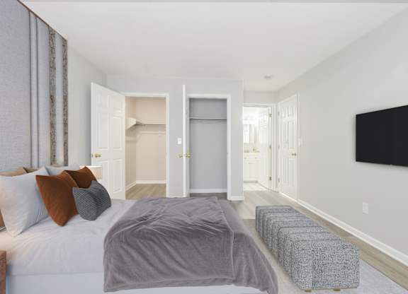 A well-lit bedroom with open closet space at The Village at Bridgewater in Bridgewater, NJ. Highlights include neutral tones, wood-style flooring, and an ensuite bathroom.
