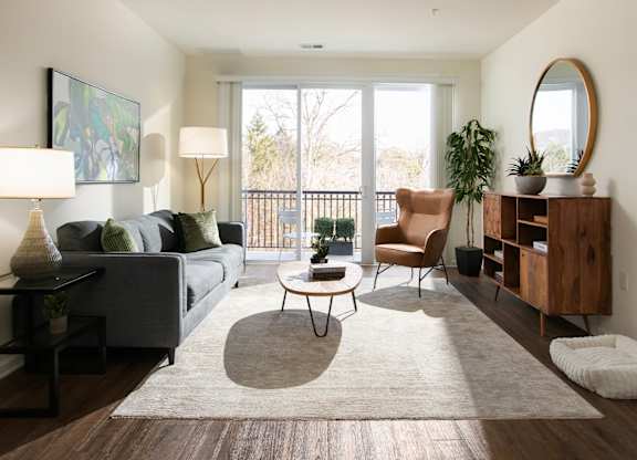 A living room with a grey couch, a coffee table, a chair, a side table, a floor lamp, a potted plant, a mirror, and a wooden cabinet.