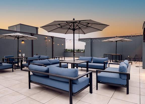 Rooftop terrace with blue cushioned seating, umbrellas, and string lights at The Botanic in Carteret, NJ