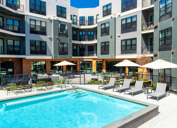 a swimming pool in front of a building with chairs and umbrellas