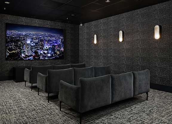 A dark room with a large screen and grey couches.