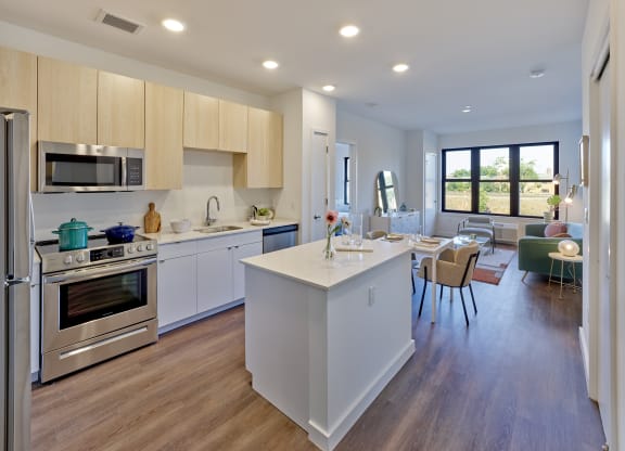 Bright kitchen and living room with an open floor plan at The Mint Rahway, featuring modern appliances, a central island, and large windows, perfect for studio apartments near Newark Airport.