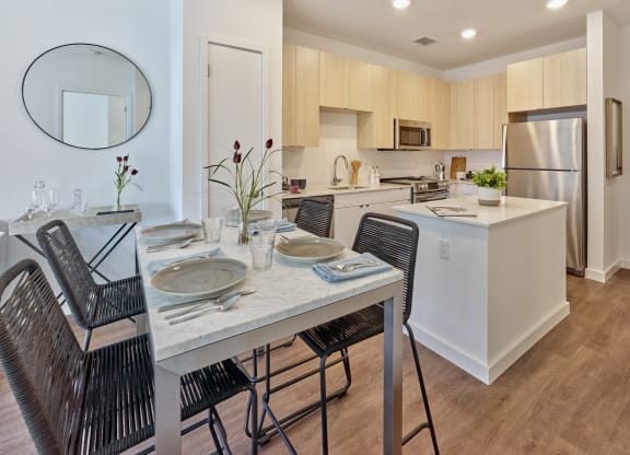 Chic dining and kitchen area at The Mint Rahway with a marble dining table, modern kitchen appliances, and light wood cabinets, ideal for open floor plan studio apartments near the Union County Performing Arts Center.