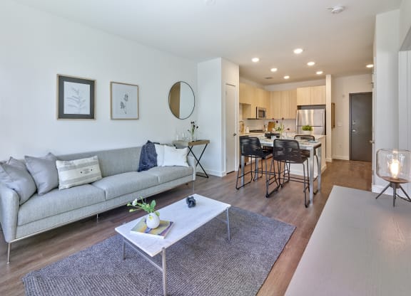 Contemporary living room at The Mint Rahway with a stylish gray sofa, a marble coffee table, and a large window, offering a comfortable space for luxury apartment rentals near the Rahway Train Station.