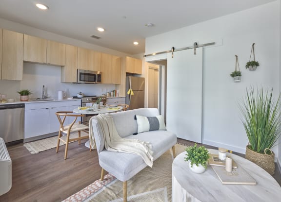 Open floor plan in a stylish living and kitchen area at The Mint Rahway, with light wood cabinets, modern appliances, and a cozy dining setup, ideal for luxury apartment rentals near the Union County Performing Arts Center.