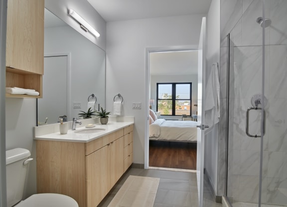 Sleek bathroom at The Mint Rahway with modern fixtures, a large mirror, and a view into a well-lit bedroom, ideal for luxury apartment rentals near Newark Airport.