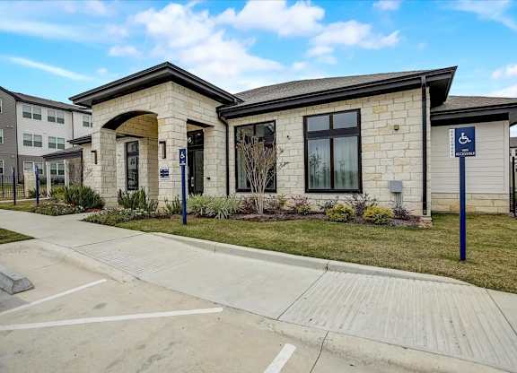 Single-story amenity building with stone façade, large windows, and neatly planted landscaping along the drive.