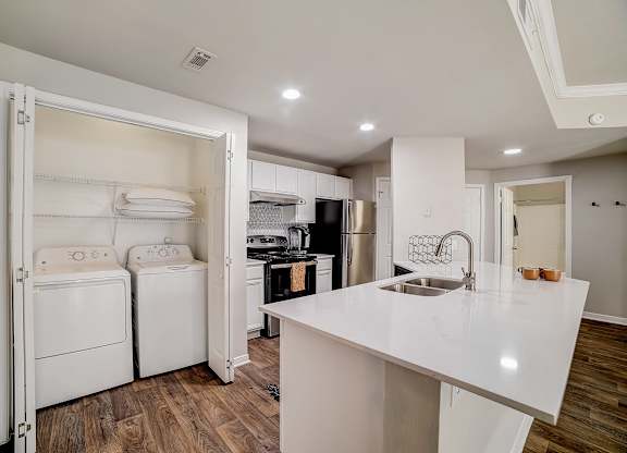 In-home laundry closet with washer and dryer beside bright kitchen island.