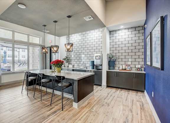 Shared clubhouse kitchen with expansive island seating, sleek cabinetry, and tall windows for daylight.