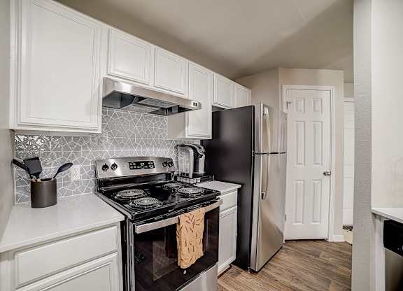White-cabinet kitchen with patterned tile backsplash, electric range, and stainless refrigerator.