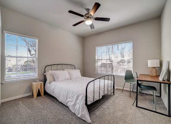 Carpeted bedroom with ceiling fan, two windows, and simple work desk.