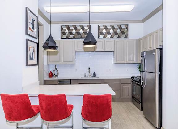 A modern kitchen with a white island and red chairs.