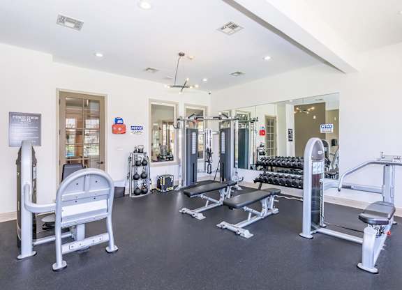 A gym with a variety of equipment including a leg press machine, a squat rack, and a bench press.