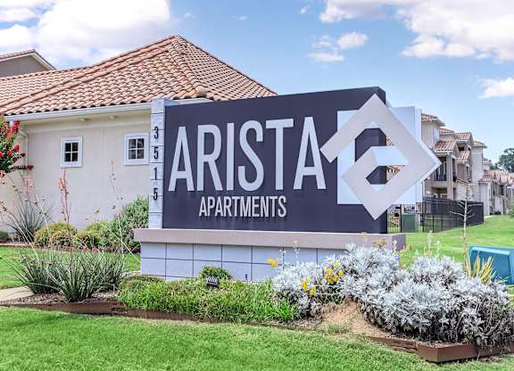 A sign for Arista Apartments is in front of a building.