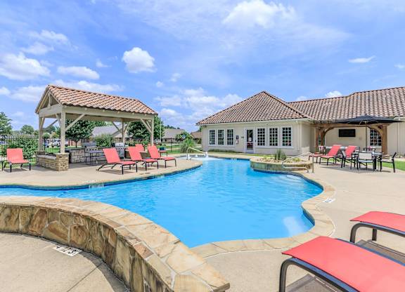 A large outdoor swimming pool with red lounge chairs and a gazebo.