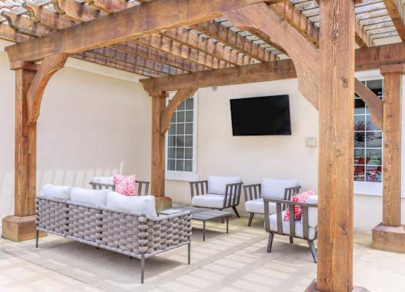 A wooden pergola with a grey sofa and chairs underneath.