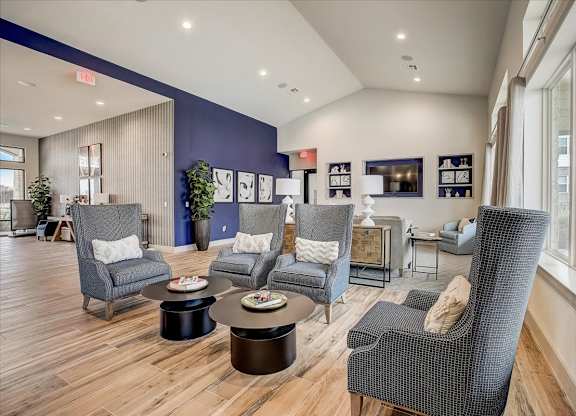 Clubhouse seating area with high-back chairs, small round tables, and sunlit windows along the wall.