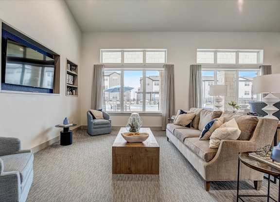 Community lounge with sofa seating, wall-mounted TV, and bright windows overlooking the courtyard.