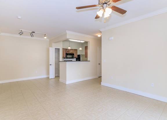 A spacious living room with a ceiling fan and a kitchen area in the background.