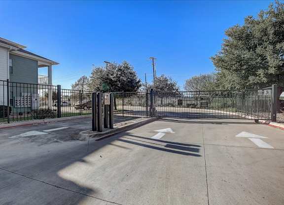Gated community entrance drive with keypad access and wide driveway.