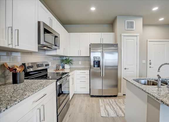 White-cabinet kitchen with granite counters, subway tile backsplash, and stainless refrigerator, range, and microwave.