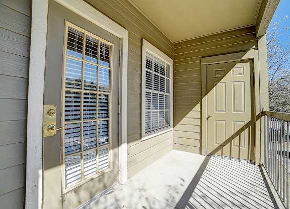 Sunny balcony with outdoor storage door, window, and railing overlooking the community.