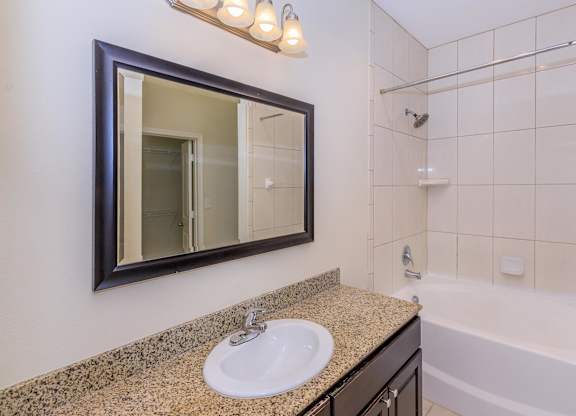 A bathroom with a sink, mirror, and bathtub.