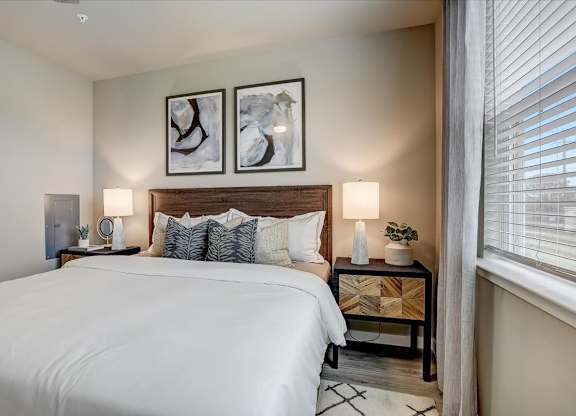 Inviting bedroom with wood headboard, bedside lamps, and a sunlit window with blinds.