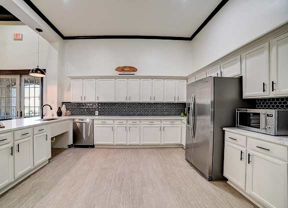 Clubhouse prep kitchen with white cabinetry, stainless refrigerator, and dark hex tile backsplash.