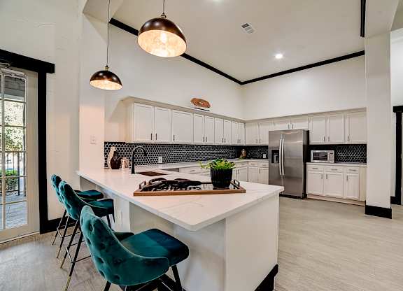 Clubhouse kitchen island with bar seating, pendant lighting, and stainless refrigerator.
