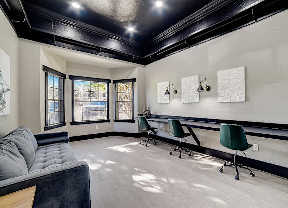 Coworking room with built-in counter, rolling chairs, and sofa seating under dark ceiling.