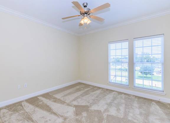 A room with a ceiling fan and two windows.